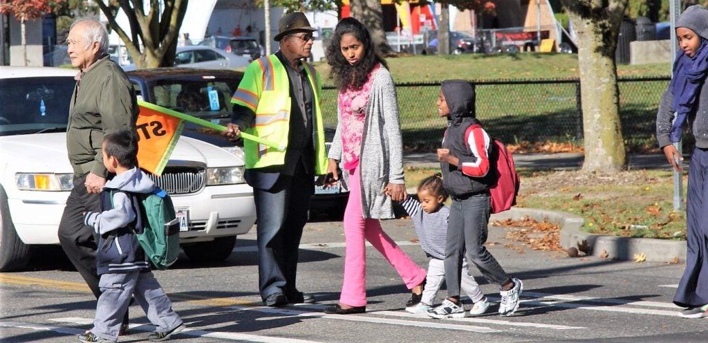 Crossing guard holds out flag as families cross the street.